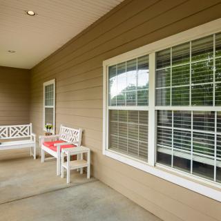 A cozy porch featuring two white benches with red cushions, next to windows with blinds.