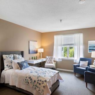 A cozy bedroom with a well-decorated interior featuring a bed, chairs, and natural light coming through the window.