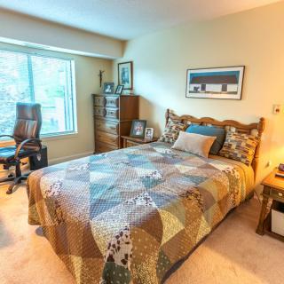 A cozy bedroom with a neatly made bed, chair, and desk near a large window.