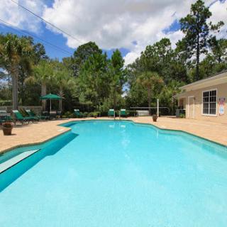 A serene poolside oasis surrounded by lush greenery and a clear blue sky.