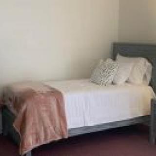 A minimalist bedroom featuring a single bed with white linens and decorative pillows.