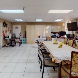 A spacious dining area featuring a long table set for meals, surrounded by comfortable chairs in a well-lit space.