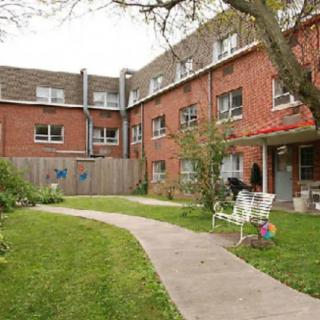 A red brick building with a garden and pathway featuring benches and trees.