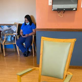 A person seated in a waiting room, engaged with their mobile phone while another chair stands prominently in the foreground.