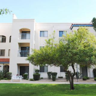 A modern apartment building with landscaped greenery and trees in front.