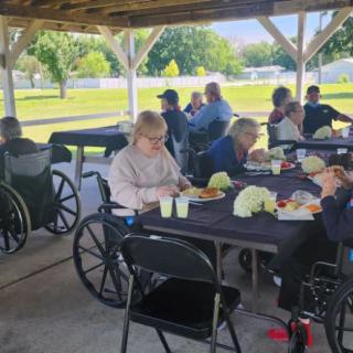 A group of people enjoying a meal together under a pavilion in a park setting.
