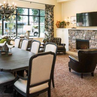 A cozy living and dining area featuring a fireplace, a large table with upholstered chairs, and a chandelier.