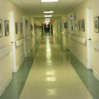 A long, brightly lit hospital corridor with doors on both sides.