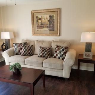 Cozy living room with a beige sofa, patterned cushions, a wooden coffee table, and decorative lamps.