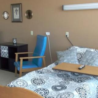 A hospital room featuring a bed with a tray, a chair, and wall decor.
