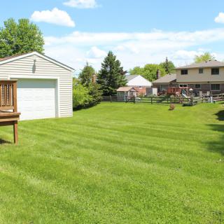 A well-maintained backyard with a large green lawn, a garage, and a house in a suburban neighborhood.