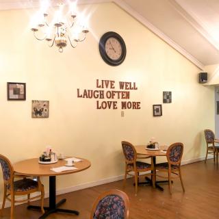 A cozy cafe interior featuring tables, chairs, decorative wall art, a chandelier, and an inspirational quote on the wall.