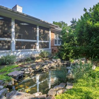 A serene garden view featuring a tranquil pond and lush greenery beside a cozy home.