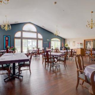 A spacious restaurant dining area with neatly arranged tables and chairs, featuring large windows and elegant chandeliers.