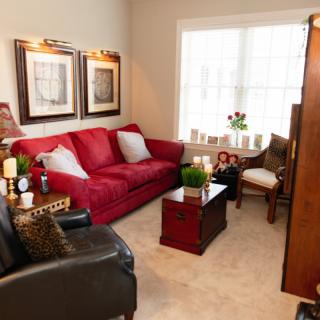 A cozy living room with a red sofa, armchairs, and a coffee table, warmly lit by natural light from a large window.