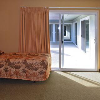 A cozy bedroom featuring a bed with a floral bedspread, adjacent to a sliding glass door leading to a sunlit patio.