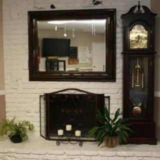 A cozy living room setting featuring a fireplace adorned with plants and candles, a large mirror above it, and a classic grandfather clock to the side.
