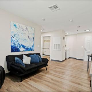 A modern living room featuring a black sofa with blue cushions, abstract artwork, and wood flooring.