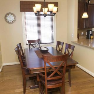 A dining room featuring a wooden table with six chairs and a chandelier, next to a window with blinds.