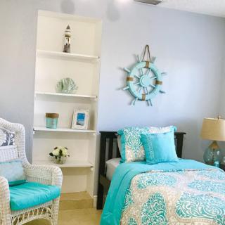A cozy bedroom with a coastal theme features blue and white decor, including patterned bedding, a decorative wall clock, a stylish lamp, and a comfortable chair.