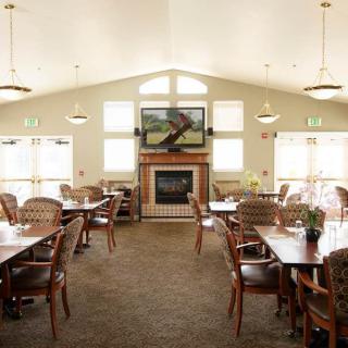 A spacious dining area with multiple tables and chairs, featuring a fireplace and large windows.