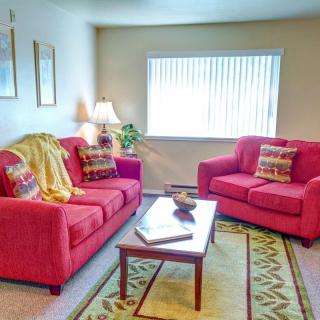 A cozy living room featuring two red sofas, a wooden coffee table, and a softly lit lamp by the window.