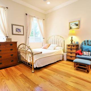A cozy bedroom with a metal-frame bed, a wooden dresser, and a comfortable chair on a hardwood floor.