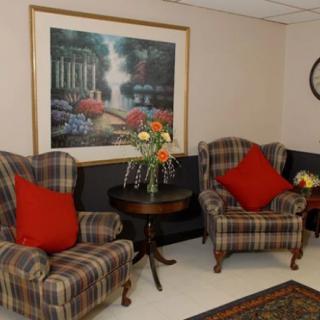 A cozy living room with plaid armchairs, red pillows, a central table with a flower vase, and a framed artwork on the wall.