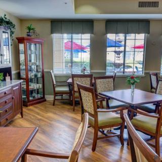 A cozy dining area with wooden tables and chairs, illuminated by natural light from large windows.
