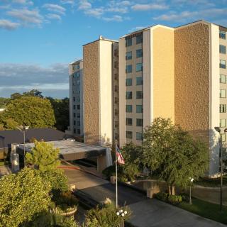 A hotel building surrounded by trees under a blue sky.