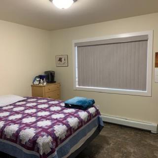 A cozy bedroom with a bed adorned with a quilt, a dresser next to it, and a window with blinds.