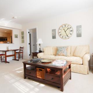 A cozy living room with a beige sofa, wooden coffee table, and large wall clock.
