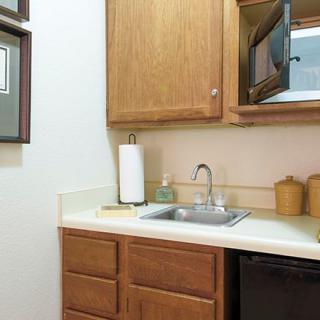 A compact kitchen space with a sink, wooden cabinets, and a countertop microwave.