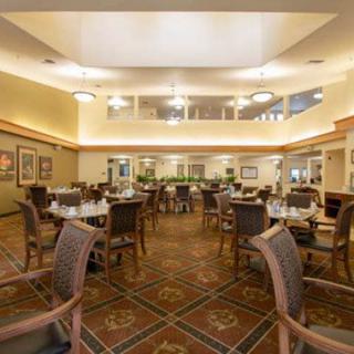 A spacious dining area with elegantly arranged tables and chairs, featuring warm lighting and a plush carpet.
