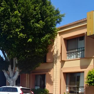 A street view of a two-story building with trees and parked cars under a clear blue sky.