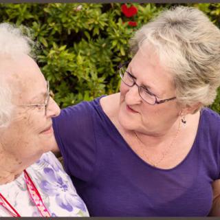 An elderly woman and another woman sharing a moment outdoors, exemplifying care and connection.