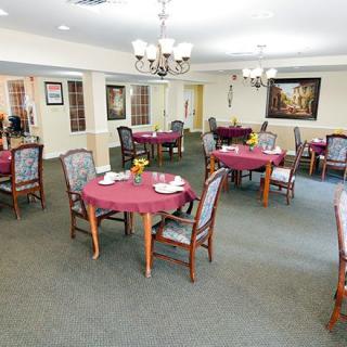 A well-set dining room with round tables, chairs, and chandeliers.