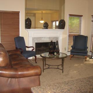 A cozy living room with a leather sofa, two blue chairs, and a glass coffee table in front of a fireplace.