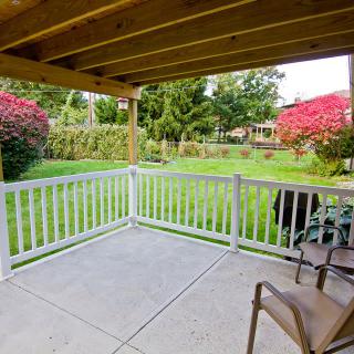 A cozy backyard patio with a white fence overlooking a lush garden.