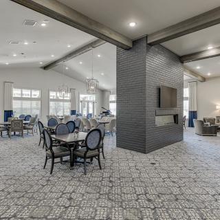 A modern dining area with elegant decor, featuring tables and chairs arranged around a central column with a mounted TV.