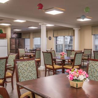 A well-lit dining area with arranged tables and chairs, featuring decorative flowers.