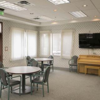 A spacious room with tables, chairs, a television, and a piano.