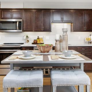 A modern kitchen with wooden cabinets and island seating, featuring stainless steel appliances.