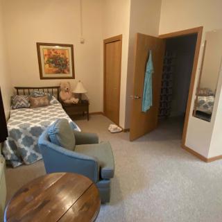 A cozy bedroom interior featuring a bed, armchair, and a small table with a view of an open closet door.