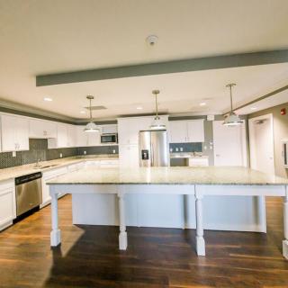 A spacious modern kitchen with an island, featuring white cabinets and pendant lighting.