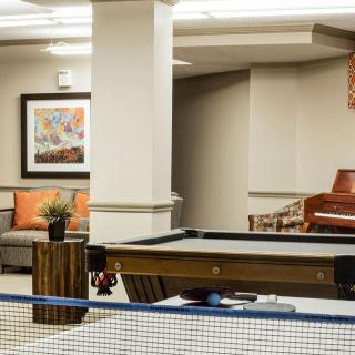 A cozy game room featuring a pool table with a ping pong net, comfortable seating, and a piano.