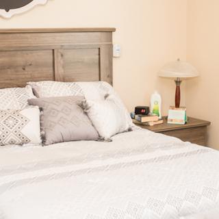 A cozy bedroom with a neatly made bed, adorned with several pillows, and a nightstand featuring a lamp and some items.