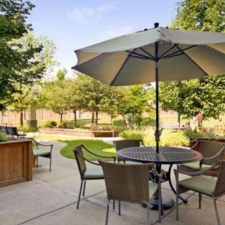 A peaceful garden patio with a table, chairs, and umbrella surrounded by lush greenery.