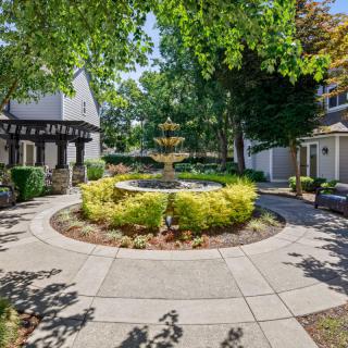 A scenic garden with a central fountain surrounded by trees and pathways.