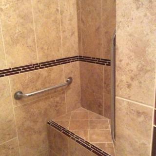 A tiled shower corner with a built-in seat and grab bar.